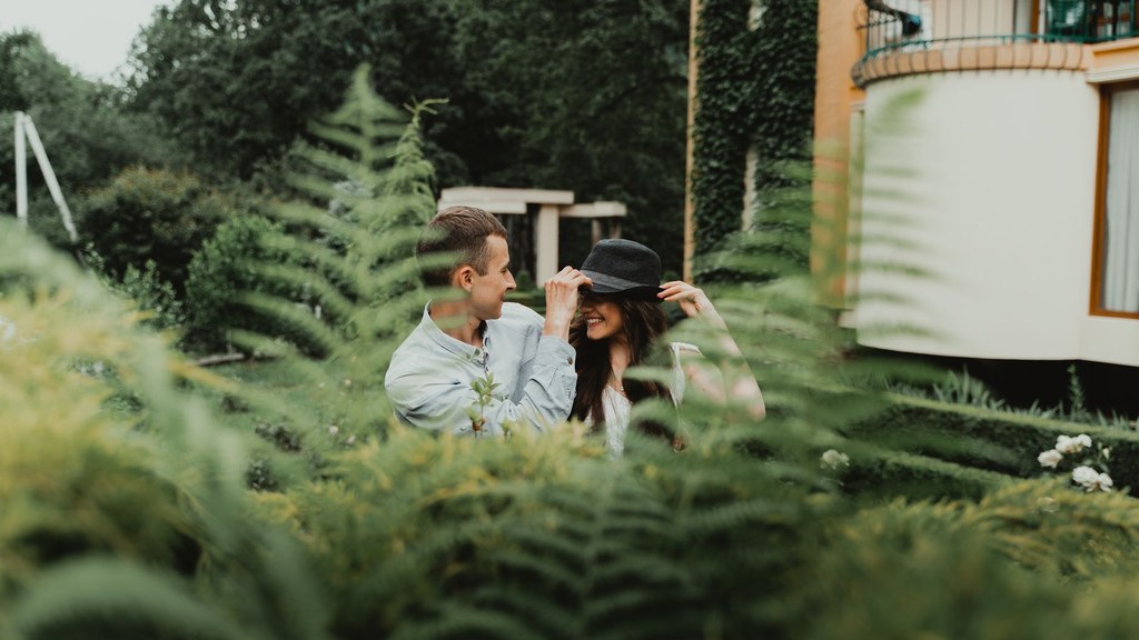Laughing couple among green ferns in a garden, showing how attachment style shapes everyday warmth and intimacy