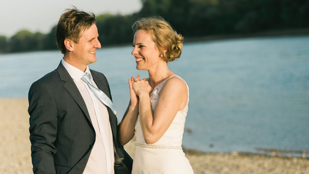 A smiling bride and groom holding hands on a sunny riverside beach, illustrating couple similarity in values and marriage