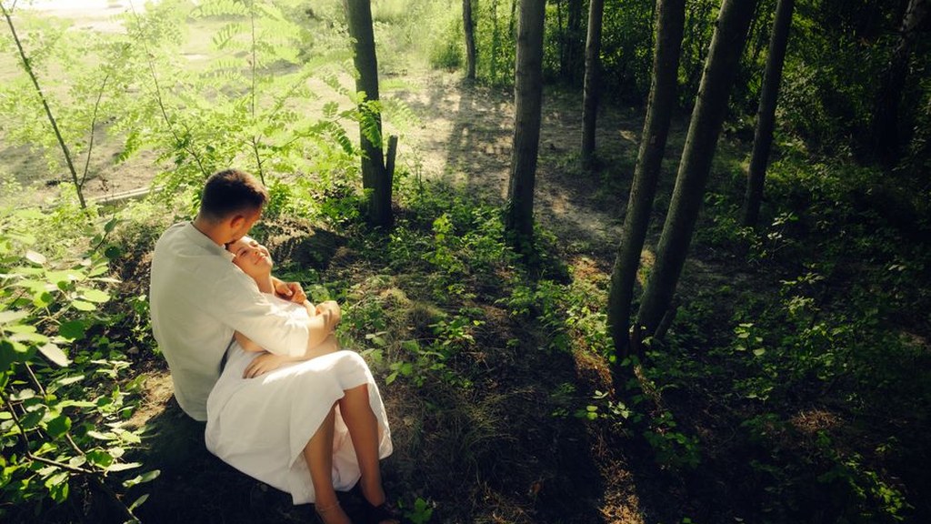 Young man holding his partner close while sitting in a sunlit forest, comfort during heartbreak and grief