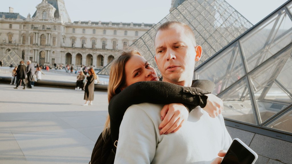 Woman hugging a man who holds his phone in Paris, a reminder of how small habits become dating dealbreakers