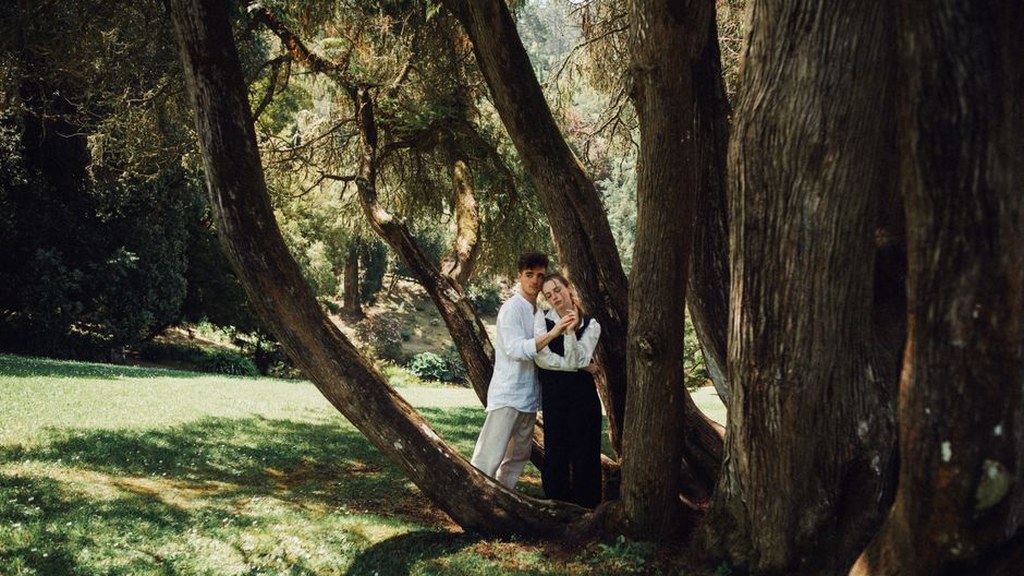 Young couple embracing beneath large trees in a sunny garden, emotional support after heartbreak