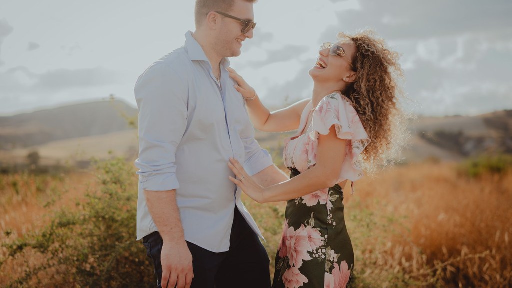 Couple laughing together in a sunny meadow, showing the playful openness that supports sexual communication