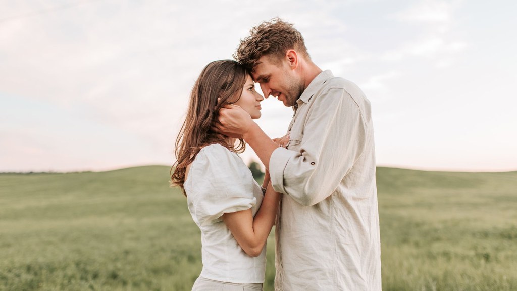 Couple style example: partners in different but harmonised cream and white outfits standing close in a sunlit green field