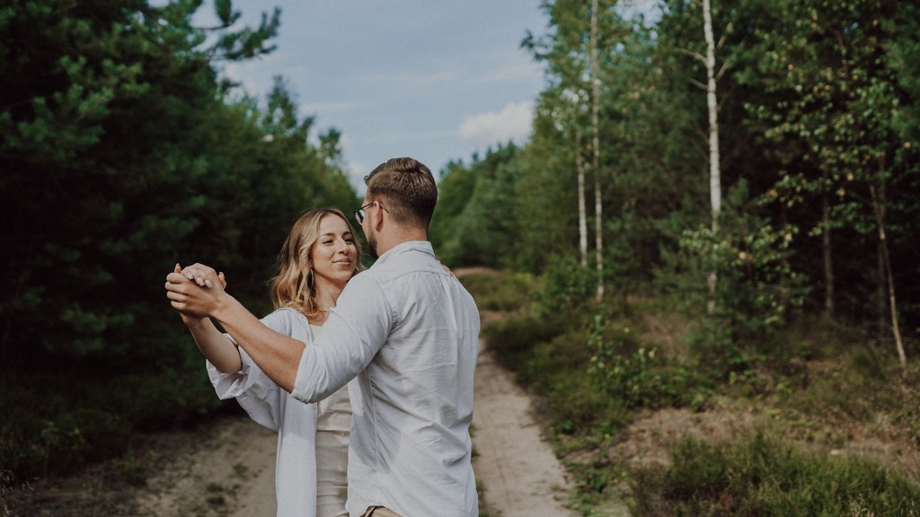 Couple style detail: partners in neutral coordinated clothes dancing hand in hand on a forest path