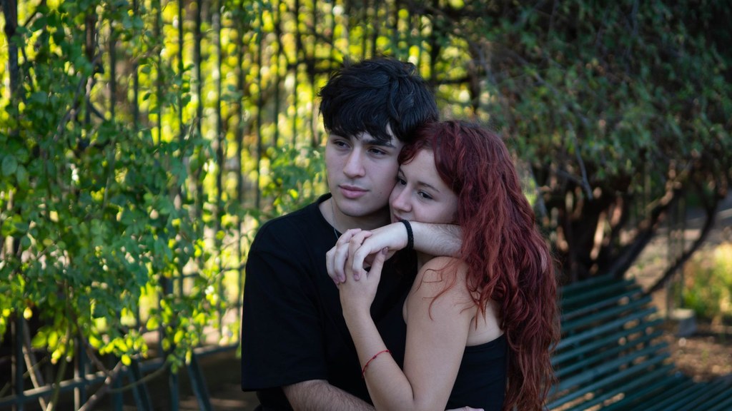 Young couple embracing on a sunny park bench after their first trip together