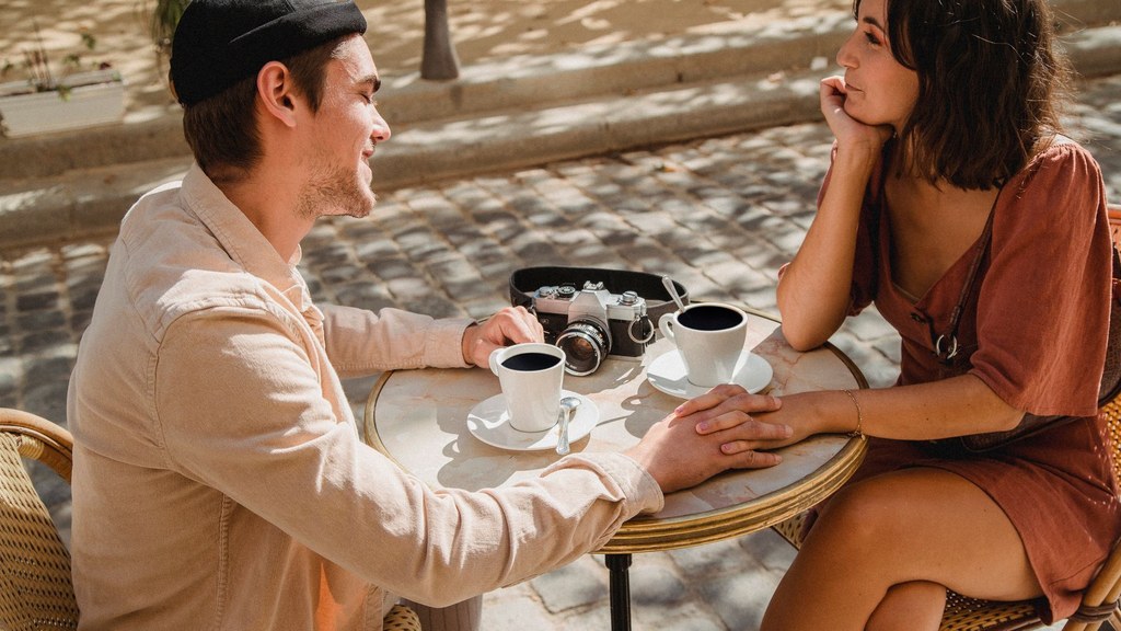 Couple in a long-distance relationship holding hands over coffee during a visit at a sunny café