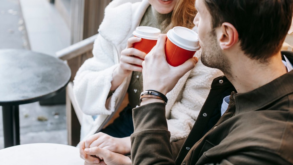 Couple holding hands over takeaway coffee on a terrace; a low-cost date and money in relationships